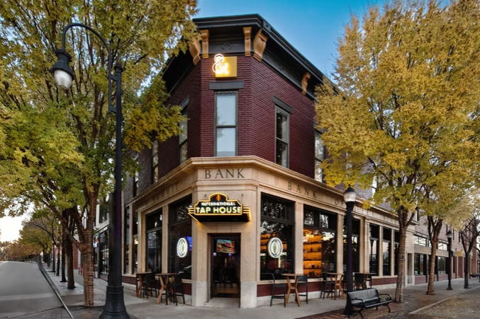exterior of an old brick bank with an international tap house neon sign